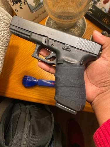 A reviewer holds a handgun showing the grip tightly wrapped with black Raid Tape.
