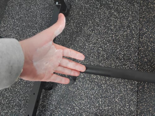 A reviewer's hand coated in The Gripper Liquid Chalk over a gym floor and near a barbell.