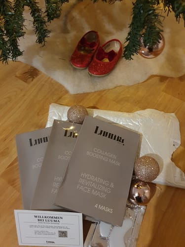 Ein Kunde zeigt die Kollagen Boosting Maske-Verpackungen mit weihnachtlicher Dekoration auf einem Holzboden.