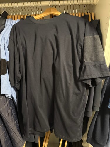 Ein Rezensent zeigt sein dunkles Defcon 5 Taktisches T-Shirt an einem Kleiderbügel in einem Schrank.