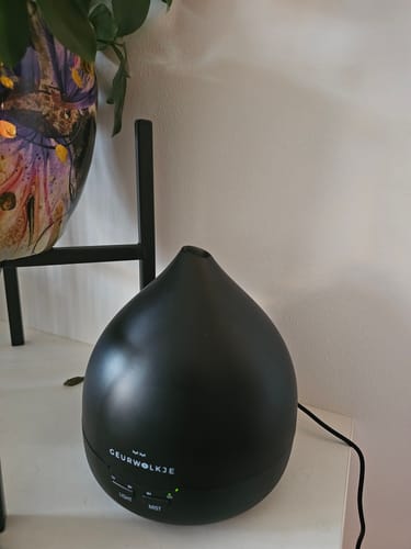 Recensent toont de matzwarte Geurwolkje aroma diffuser, die aan staat op een wit meubelstuk.