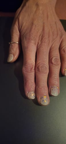 Hand einer Kundin, die die hellen, glitzernden UV-Gel-Nagelfolien 'Lush Lilac' auf kurzen Nägeln trägt.