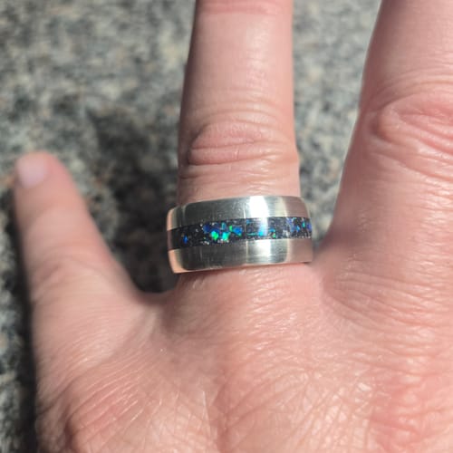 Customer's hand wearing the silver Cremation Ash Coin Ring with a dark inlay and vibrant opal flecks.