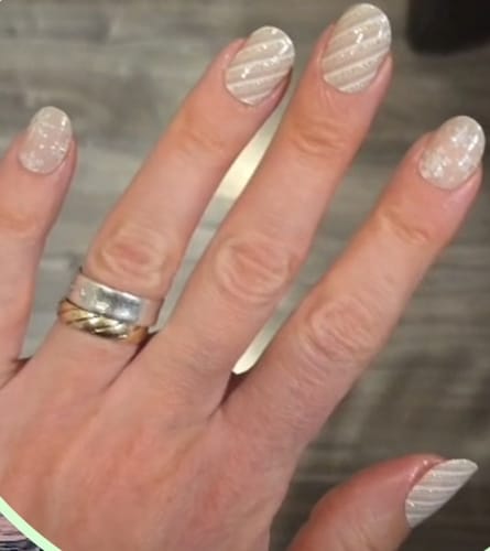 Hand einer Kundin mit Blush Wonderland UV-Gelfolien, die ein glitzerndes Streifen- und Schneeflocken-Design zeigen.