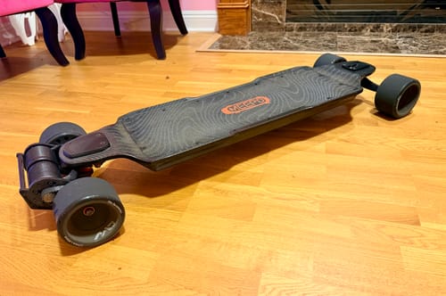 Customer's well-used MEEPO Vader - Hurricane Carbon electric skateboard resting on a light wood floor indoors.