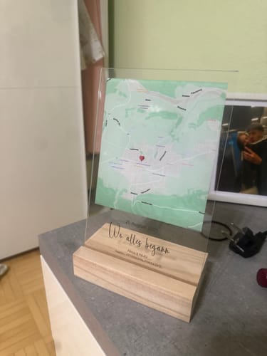 Ein Kunde zeigt seine personalisierte Acryltafel mit einer Karte auf einem Holzsockel, die auf einer Kommode steht.