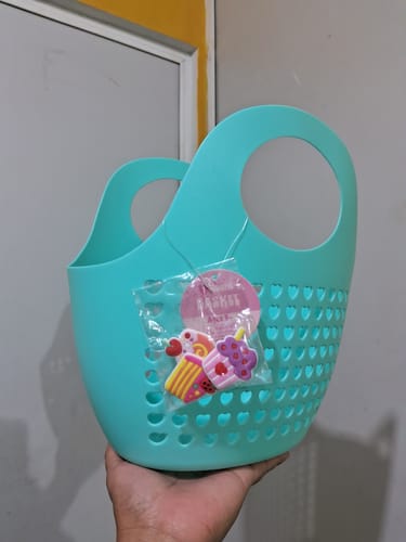 Una clienta sostiene en la mano la cesta de juguete azul, que tiene perforaciones en forma de corazón y adornos de pastelitos.