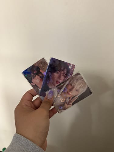 Customer holding three photocards fanned out, each in a premium holographic sleeve.