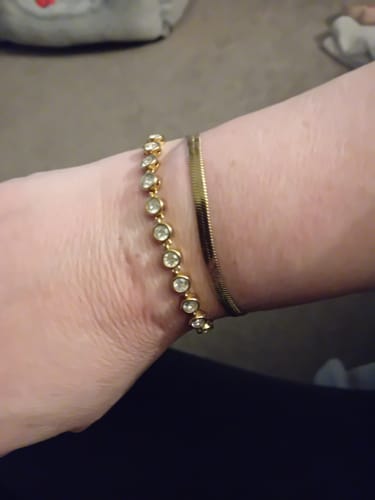 Reviewer's wrist showing the gold Essentials Bracelet stacked next to a jeweled bracelet.