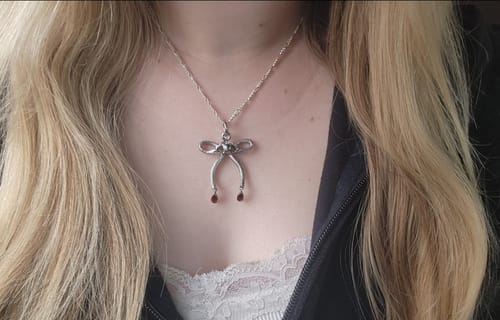 A reviewer wearing the silver Eve's Pendant on a delicate chain against their chest, showing off the detailed design.