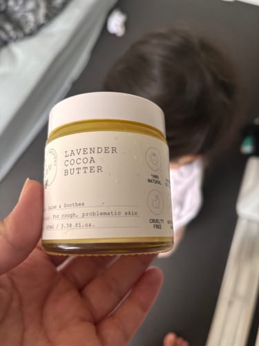 Customer holding a jar of Lavender Cocoa Butter, with a child visible in the background.