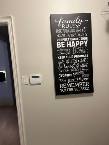 Customer's vertical 'Family Rules' Framed Canvas with white text hanging on a wall in their laundry room.