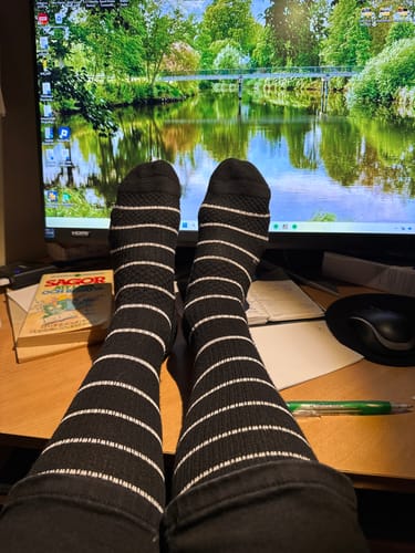 Kundens svarta, vitrandiga Diasocks stödstrumpor på fötterna som vilar på ett skrivbord.