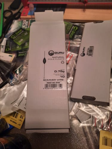 Recensent toont de verpakking van de Guru Skimmer Wire dobbers tussen ander visgerei.