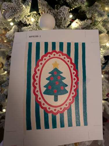 Reviewer holding their completed Mini Painting of a Christmas tree in a decorative frame in front of a Christmas tree.
