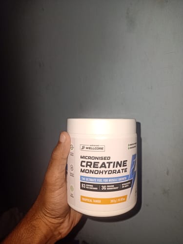 Reviewer holding a white tub of Wellcore Pure Micronised Creatine Monohydrate in the Tropical Tango flavor.