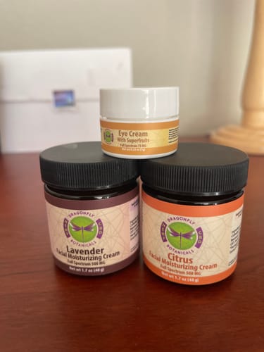 Reviewer's jar of Citrus Facial Moisturizing Cream next to the Lavender cream and a small jar of Eye Cream on a wooden table.