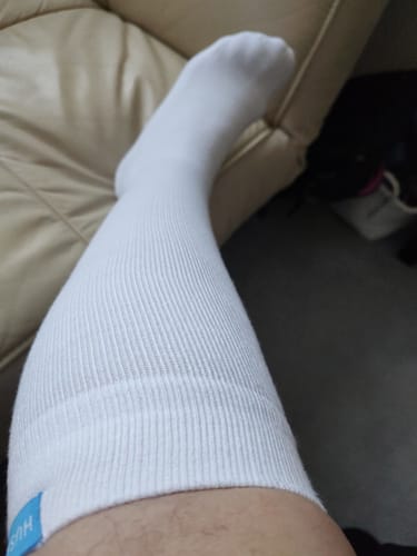Customer wearing a white Performance Eucalyptus Compression Sock while resting their leg on a couch.