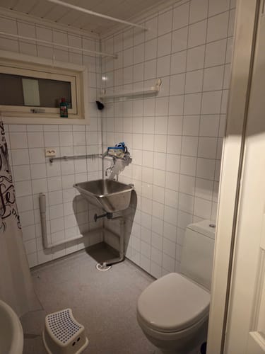Anmelders vaskerom med hvite fliser og stålvask før renovering.