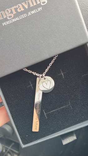 Reviewer showing their personalized Orbis necklace with engraved bar and heart disc pendants in its box.