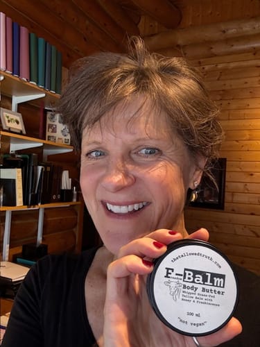 Reviewer smiling while holding up a round, black tin of F-Balm Body Butter.