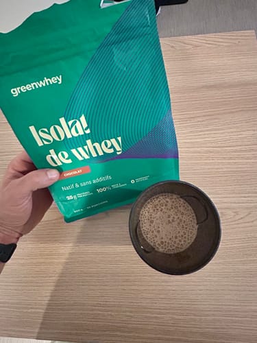 Un client tient le sachet d'Isolat de Whey Native à côté d'un bol contenant la boisson protéinée préparée.