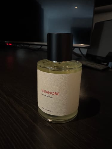 Customer's Eleanore perfume bottle with a white label and black cap on a dark table.