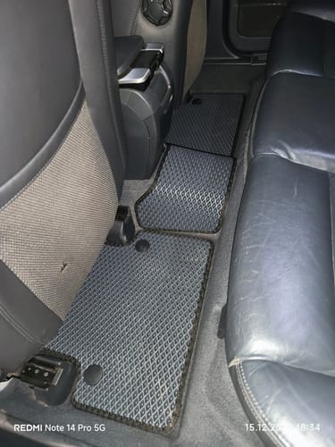 Recenzent pokazuje ciemne dywaniki samochodowe z wzorem w romby, dopasowane do tylnej podłogi samochodu.