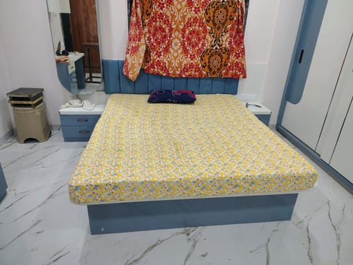 Customer's Flo Mattress Ortho with a yellow patterned cover, placed on a light blue bed frame in a bedroom.