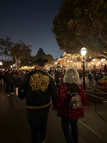 Reviewer seen from behind wearing the black Scrooge and Marley Coach Jacket with gold embroidery at a theme park at night.