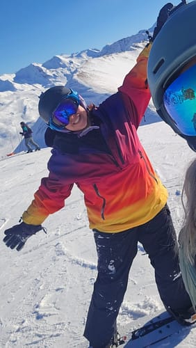 Reviewer smiling on a snowy mountain, wearing the colorful Sunset Gradient Snow Anorak.
