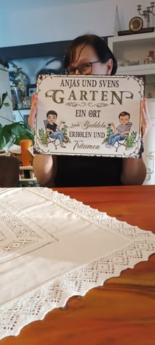 Eine Kundin hält ihr personalisiertes Gartenschild mit den Namen und Illustrationen von zwei Personen.
