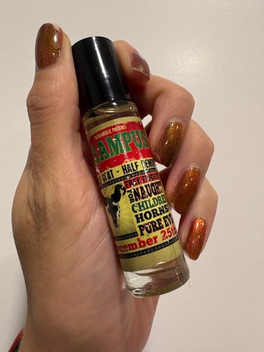 Customer's hand with sparkly copper nails holding a Krampus rollerball perfume bottle.