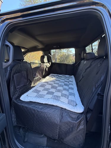 Customer's car seat hammock cover installed in the back of a large truck, with a quilt on top.
