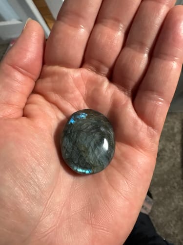 Customer holding a polished, round Labradorite crystal in the palm of their hand, showing a flash of blue color.