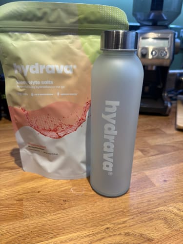 Customer's pouch of Hydrava Electrolyte Salts next to a matching branded water bottle on a wooden countertop.
