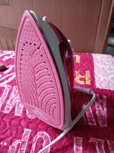 Cliente mostrando la suela de cerámica rosa de la plancha de vapor Oster sobre una tela estampada.