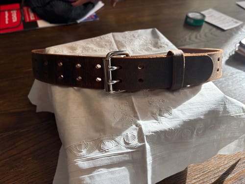 Customer's dark brown Woodstock Double Prong belt coiled on a table, showing the thick leather and silver buckle.