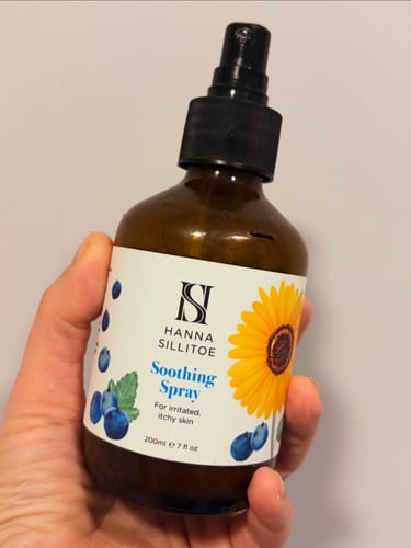Customer holding the brown bottle of Soothing Spray, showing its white label and black nozzle.