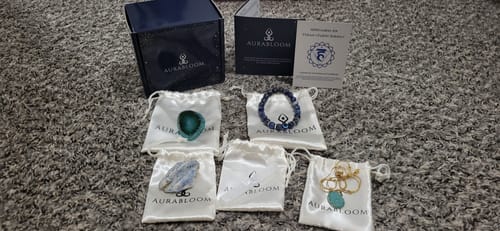 Customer's unboxing of the AuraBloom Subscription Box, showing a blue bracelet, necklace, and loose crystals on their pouches.