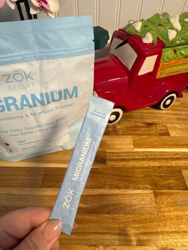 Customer's hand holding a single-serving packet of Migranium with the larger product pouch in the background.