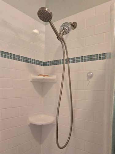 Reviewer's stainless steel 1-Spray Handheld Shower Head Set installed in a white tiled shower.