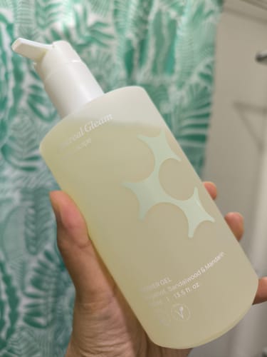 Customer holding the Ethereal Gleam Shower Gel in a frosted pump bottle in a bathroom.