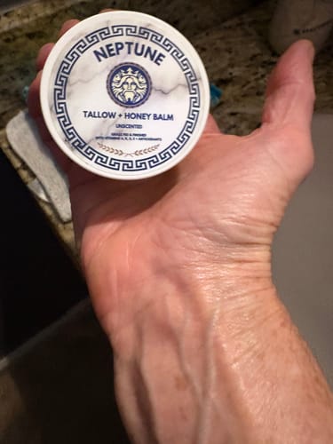 Customer holding a container of Grass Fed Tallow & Honey Balm over their hand, which has a hydrated glow.