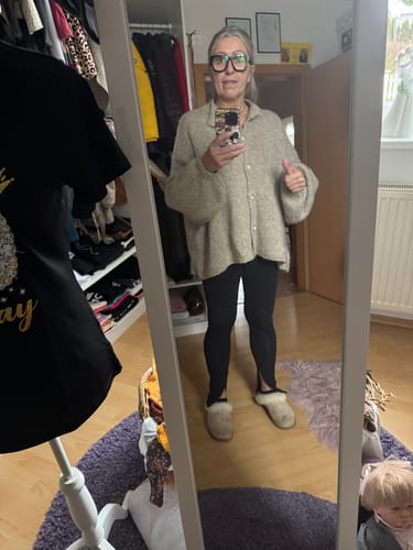 Kundin in einer Spiegelaufnahme, die den cremefarbenen Oversized Cardigan "CozyGlam" mit schwarzen Leggings trägt.