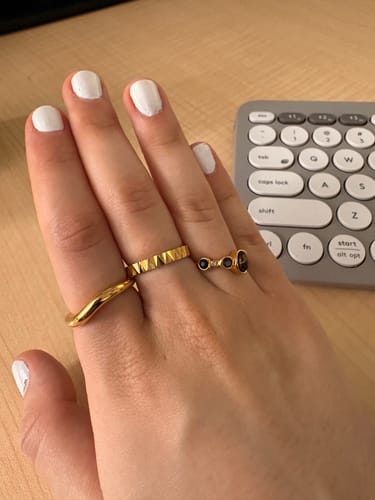Customer's hand wearing the Mina Gold Wave Ring on the pinky finger, stacked with two other gold rings.