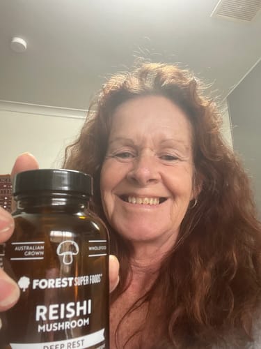 Customer smiling while holding a brown bottle of Australian Grown Reishi Mushroom Capsules.