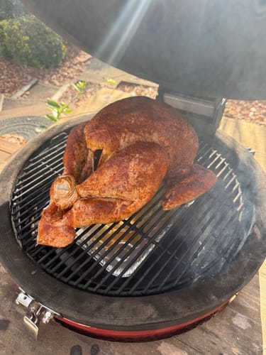 Reviewer's seasoned turkey, prepared with the Turkey Brine Kit, smoking on a round grill outdoors.