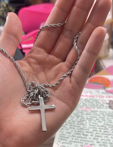 Cliente mostrando el Crucifix Pendant plateado y su cadena de cuerda en la mano.