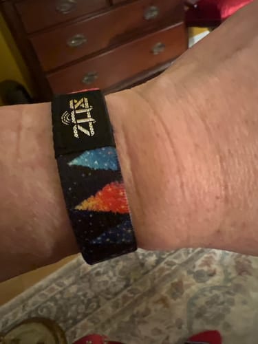 A customer wearing the Never Alone Bible Verse Bracelet on their wrist, showing its colorful mountain and space design.